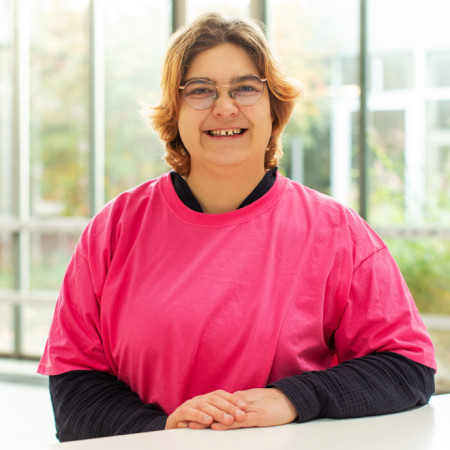 Julia Wedau lächelt in die Kamera und hat ein pinkfarbenes T-Shirt an.