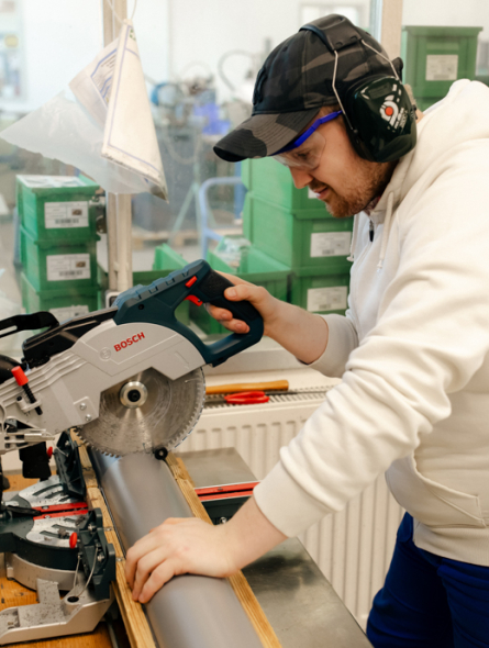 Ein Mann mit Ohrschützern sägt ein Rohr mit einer Maschine.