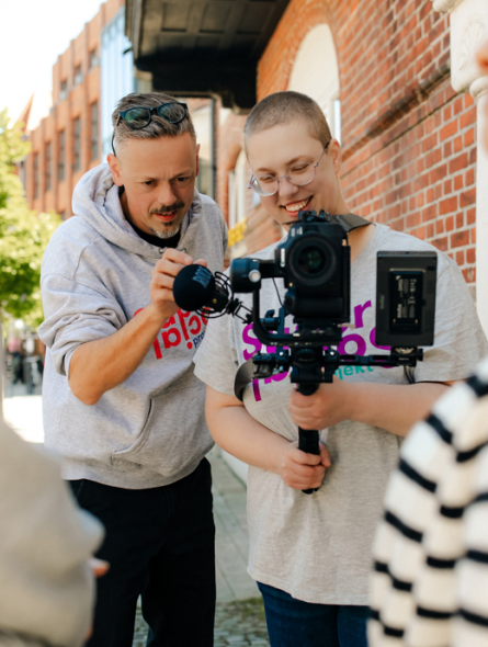 Ein Mann und eine junge Frau schauen beim Fotografieren gemeinsam in die Kamera.