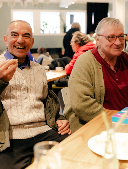 DünAmo Café: zwei Männer sitzen am Tisch, unterhalten sich und lächeln.