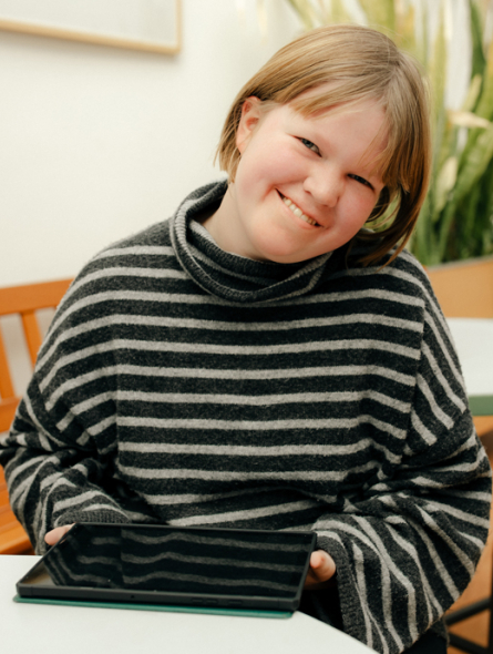 Eine junge Frau sitzt mit einem Tablet an einem Tisch