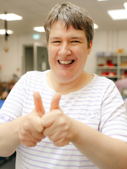 Eine Frau lächelt in die Kamera und hält ihre Daumen hoch. 