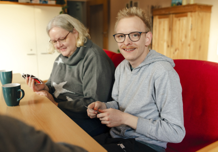 Eine ältere Frau und ein junger Mann mit Behinderung sitzen an einem Tisch und spielen Karten.