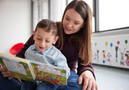 Eine junge Frau liest mit ein Jungen mit Behinderung im Kindergartenalter ein Buch.