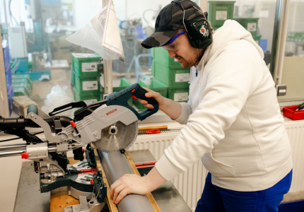Ein Mann mit Ohrschützern sägt ein Rohr mit einer Maschine.