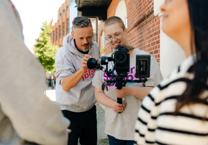 Ein Mann und eine junge Frau schauen beim Fotografieren gemeinsam in die Kamera.