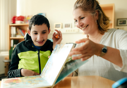 Eine Schulassistenz schaut mit einem Jungen ein Buch an.