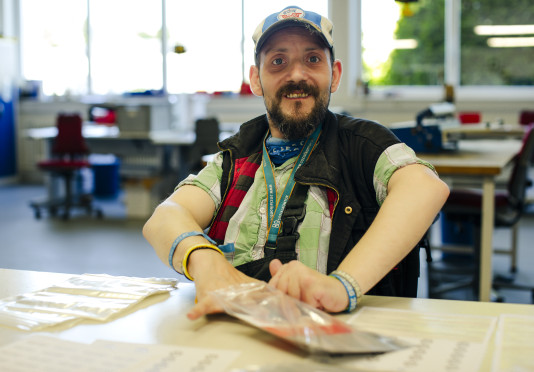 Ein Mann arbeitet in der Montage der Lebenshilfe Lüneburg-Harburg und lächelt in die Kamera. 