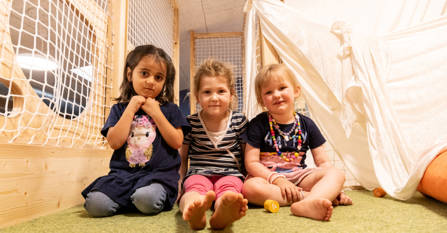 Drei Kleinkinder sitzen auf einer grünen Matte nebeneinander und schauen in die Kamera.