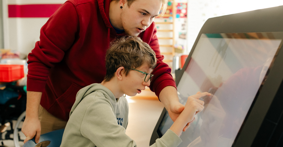 Ein Mann hilft einem Jungen mit Behinderung an einem großen Tablet.