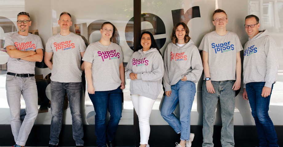 Gruppenfoto des Super Social Teams. Alle tragen ein graues T-Shirt mit dem Schriftzug SuperSocial.