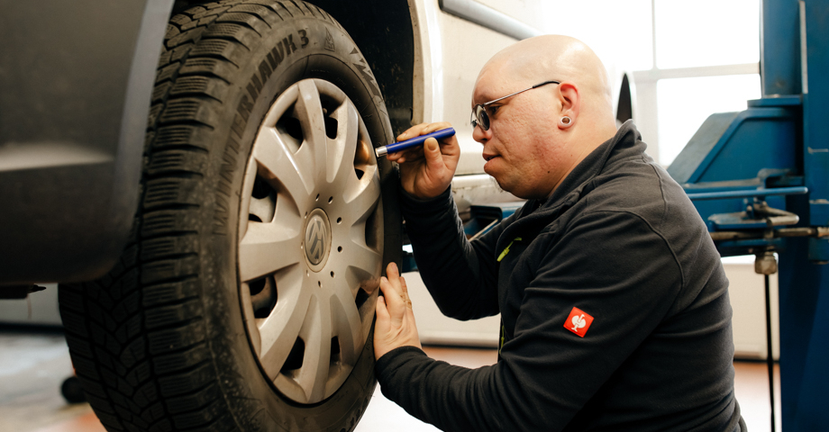 Ein Mann prüft den Reifen eines Autos. 