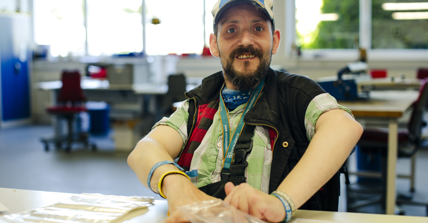 Ein Mann arbeitet in der Montage der Lebenshilfe Lüneburg-Harburg und lächelt in die Kamera. 