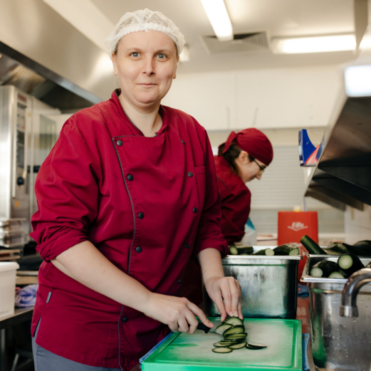 Eine Frau arbeitet in der Großküche und schneidet Gurken. 