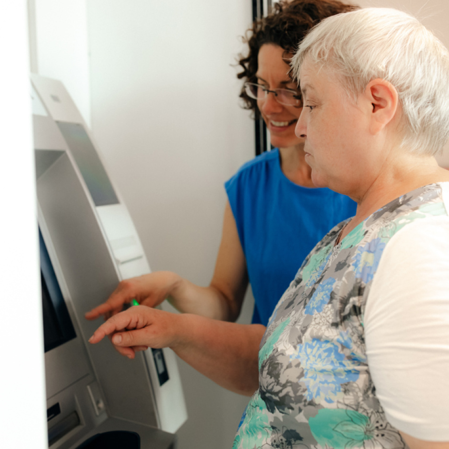 Eine Frau unterstützt eine andere Frau am Bankautomaten. 